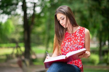 Parktaki açık havada kitap yazan genç bir kız öğrenci.