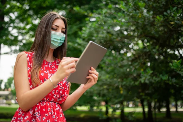 公園でタブレットを使用してマスクの若い女性 — ストック写真