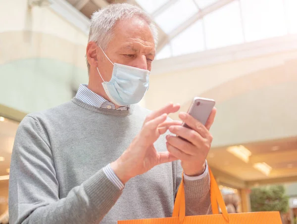 Masked elder man using his smartphone during coronavirus or covid-19 pandemic