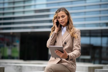 Genç iş kadını elinde tablet tutarken cep telefonunu kullanıyor.