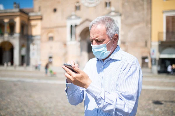 マスク男使用彼のスマートフォン屋外で大規模なヨーロッパの広場 — ストック写真