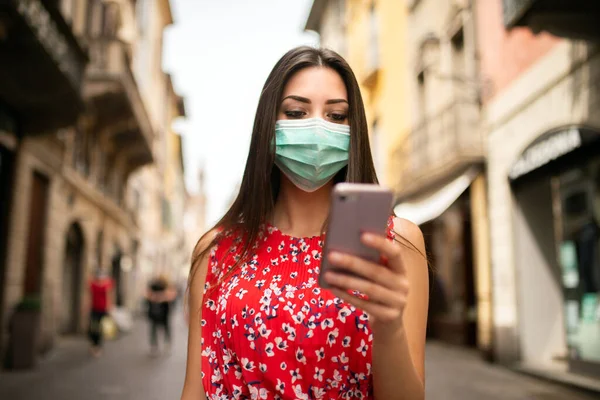 Mujer Joven Enmascarada Caminando Una Ciudad Mientras Usa Teléfono Móvil —  Fotos de Stock