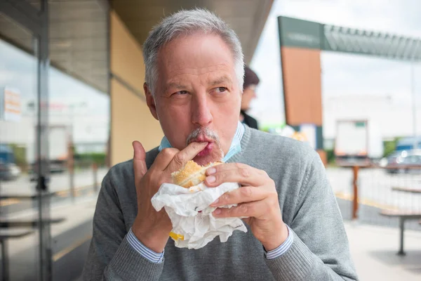 男人吃他的快餐午餐汉堡包的时候 下巴上戴着面具 这就是 验尸官 的概念 — 图库照片