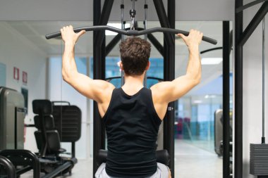 Adam spor salonunda omuzlarını ve sırtını çalıştırmak için düz makine kullanıyor. Vücut geliştirme ve doğal fitness konsepti.