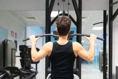 Adam spor salonunda omuzlarını ve sırtını çalıştırmak için düz makine kullanıyor. Vücut geliştirme ve doğal fitness konsepti.