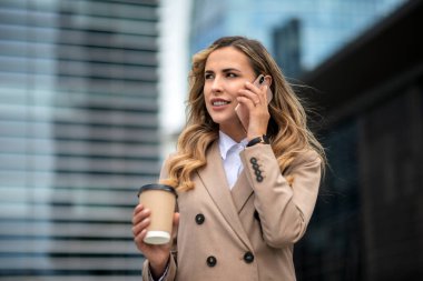 Sarışın genç iş kadını şehir caddesinde telefonla konuşuyor.