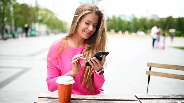 Šťastná Mladá Žena Pití Kávy Venku Při Použití Svého Smartphonu — Stock fotografie