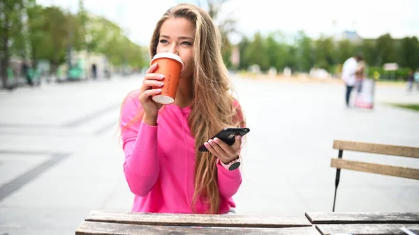 Szczęśliwa Młoda Kobieta Pije Kawę Świeżym Powietrzu Podczas Korzystania Smartfona — Zdjęcie stockowe