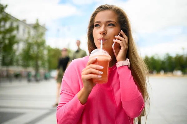 幸せな若い女性が電話で話している間にコーヒーを屋外で飲む — ストック写真