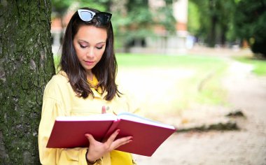 Güzel bayan öğrenci açık havada kitap okuyor.