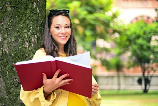 Güzel bayan öğrenci açık havada kitap okuyor.