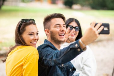 Bir grup mutlu arkadaş parkta selfie çekiyorlar.