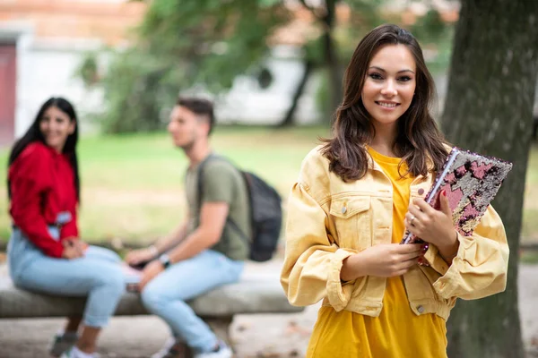 Kobieta Student Trzyma Książkę Przed Grupą Przyjaciół Parku — Zdjęcie stockowe