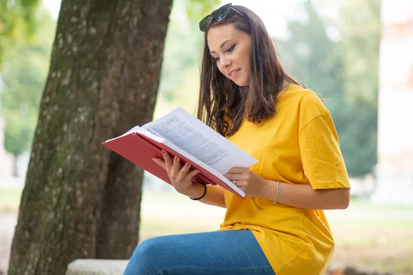 Woman student holding a book in front a a group of friends in park