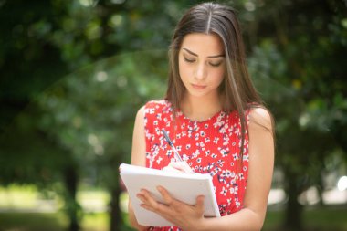 Okulun önündeki parkta ders çalışan bir kız öğrencinin portresi.