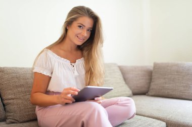 Evindeki kanepede dinlenirken tablet kullanan bir kadın.