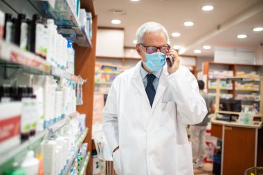 Eczanesinde yürürken telefonda konuşan maskeli eczacı. Coronavirus konsepti.