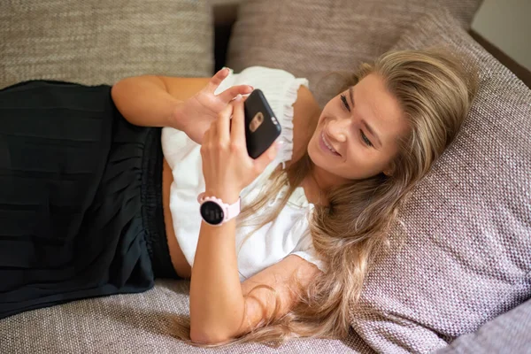 彼女のアパートでソファでリラックスしながら スマートフォンを使用して女性 — ストック写真