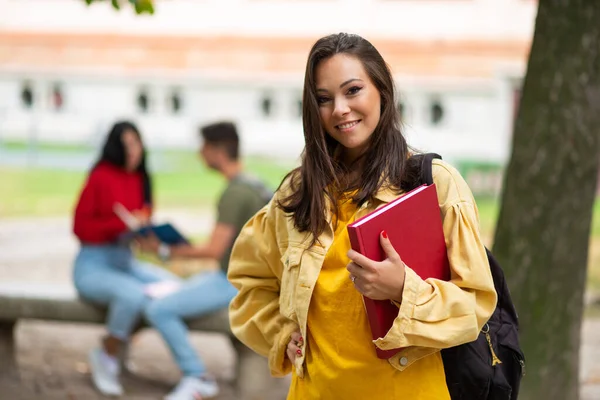 Woman student holding a book in front a a group of friends in park