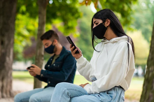 Молодые Люди Используют Свой Смартфон Время Ношения Маски Открытом Воздухе — стоковое фото