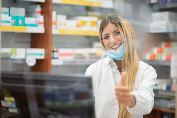 Portret Uśmiechniętego Młodego Farmaceuty Aptece Dającego Kciuki Szkło Koncepcja Koronawirusa — Zdjęcie stockowe
