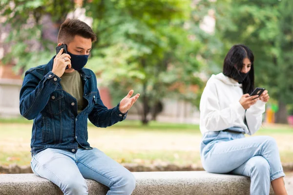 屋外でマスクをしながらスマートフォンを使う若者たち コロナウイルスや社会的距離感の概念 — ストック写真