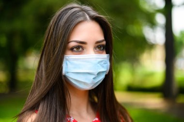 Coronavirus zamanlarında parkta maske takan güzel bir kadının portresi.