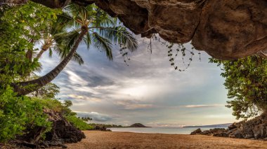Bir plajda güzel Güney Maui onu çevreleyen yemyeşil bitki örtüsü ve palmiye ağaçları ile küçük bir mağara. Maui, Hawaii, ABD.