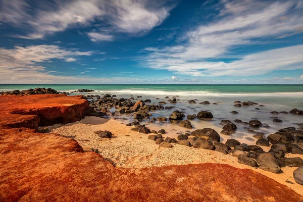 Maui Red Dirt at Baby Beach. Very colorful scene with the red dirt, gold beach, black lava rocks, green sea and blue sky. Maui, Hawaii.