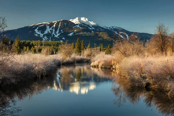 Huzur, nehir altın hayalleri güzel bir bahar sabahı Whistler dağ yansıması ile. Güneşin sadece dağın üzerinde gül ve biraz buzlu Nehri'nin aydınlatmaya başlamış. Whistler, British Columbia, Kanada