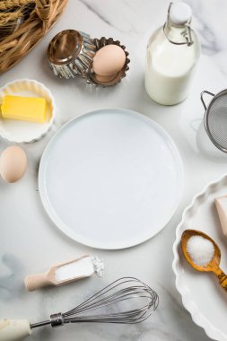 Beyaz mermer zemin, yumurta, süt kavanozu, şeker, un, tereyağı ve kabartma tozu üzerine tatlı pişirme malzemeleri. Kurabiye ya da kek pişirme telaşı. Beyaz yuvarlak ortadaki metin için maket yap, boşluğu kopyala