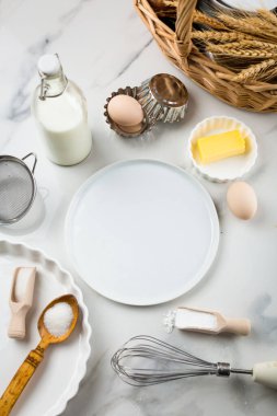 Beyaz mermer zemin, yumurta, süt kavanozu, şeker, un, tereyağı ve kabartma tozu üzerine tatlı pişirme malzemeleri. Kurabiye ya da kek pişirme telaşı. Beyaz yuvarlak ortadaki metin için maket yap, boşluğu kopyala