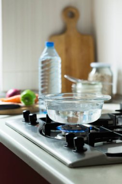 Ev yapımı çorba pişirmek için cam kasede saf içme suyu. Malzemeler mutfaktaki sobanın yanında masanın üzerinde. Düzgün yemek, temiz ve sağlıklı beslenme konsepti