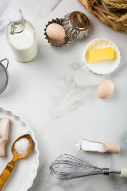 Beyaz mermer zemin, yumurta, süt kavanozu, şeker, un, tereyağı ve kabartma tozu üzerine tatlı pişirme malzemeleri. Kurabiye ya da kek pişirme telaşı. Beyaz yuvarlak ortadaki metin için maket yap, boşluğu kopyala