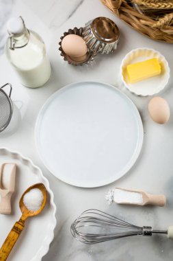 Beyaz mermer zemin, yumurta, süt kavanozu, şeker, un, tereyağı ve kabartma tozu üzerine tatlı pişirme malzemeleri. Kurabiye ya da kek pişirme telaşı. Beyaz yuvarlak ortadaki metin için maket yap, boşluğu kopyala