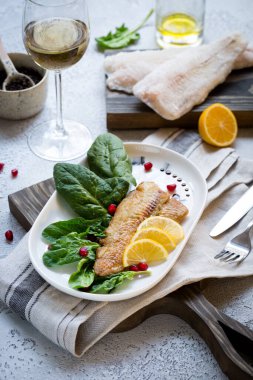 Tilapia balığı kızartılmış ve taze ıspanak yaprakları ve beyaz şarapla servis edilen limon dilimleri ile servis edilmiş. Donmuş balık parçaları ile sağlıklı ev yapımı gıda konsepti. Boşluğu kopyala