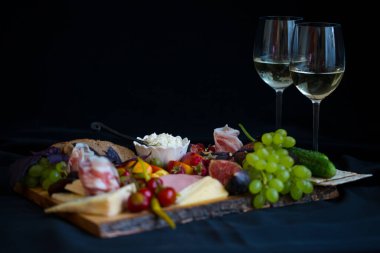 İki beyaz şarap bardağı içinde peynir tabağı ve meyve ve et.