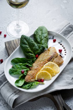 Tilapia balığı kızartılmış ve taze ıspanak yaprakları ve beyaz şarapla servis edilen limon dilimleri ile servis edilmiş. Donmuş balık parçaları ile sağlıklı ev yapımı gıda konsepti. Boşluğu kopyala