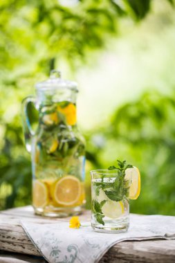 Cam sürahide ev yapımı limonata ve bahçe arka planında ahşap masada limon.