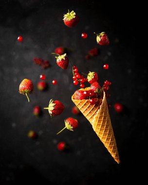 Gofret külahından kırmızı böğürtlen patlaması, meyve havalanması, koyu arka planda sağlıklı çiğ gıda kavramı.