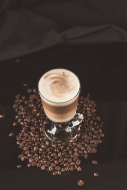 Siyah ayna arka planında kahve çekirdekleri olan bir bardak macciato latte. Kakaolu sütlü köpüklü kapuçino. Seçici odak, boşluğu kopyala