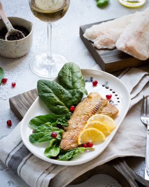 Tilapia balığı kızartılmış ve taze ıspanak yaprakları ve beyaz şarapla servis edilen limon dilimleri ile servis edilmiş. Donmuş balık parçaları ile sağlıklı ev yapımı gıda konsepti. Boşluğu kopyala