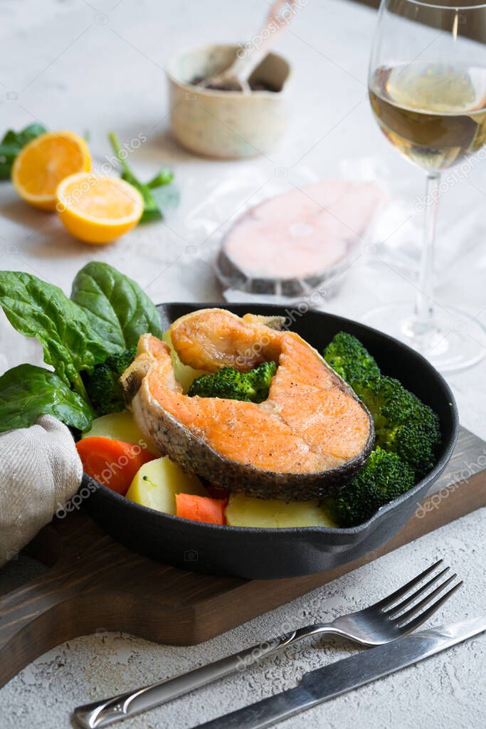 Grilled or fried salmon piece with vegetables, green spinach leaves, broccoli, potato and carrots with glass of white wine. Healthy home made food concept, selected focus