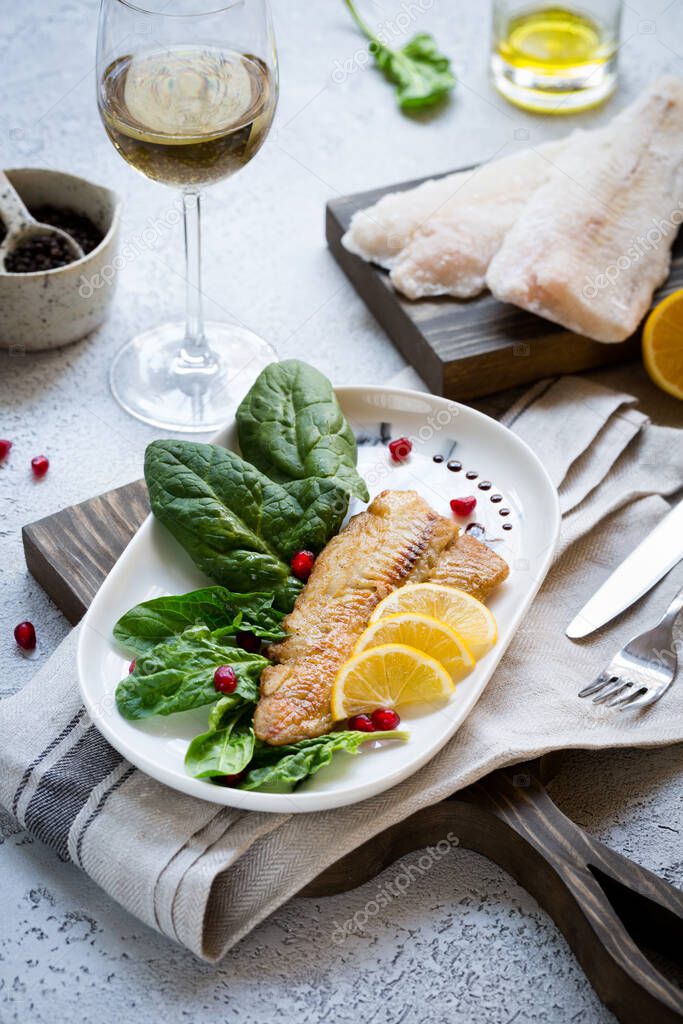 Tilapia fish fried and served with fresh spinach leaves and lemon slices served with white wine. Healthy home made food concept with frozen fish pieces. Copy space