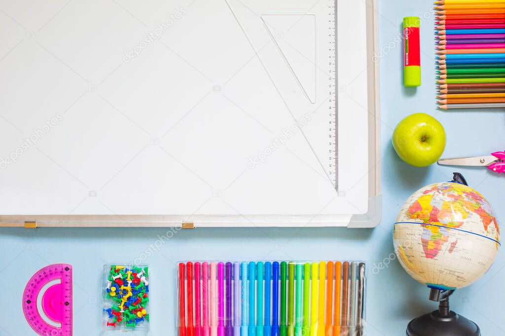 School art supplies concept on blue background globe, markers, pencils, glue stick, scissors, stationary pins, apples, rules, pens, playdough, blank notebook, back to school flat lay copy space