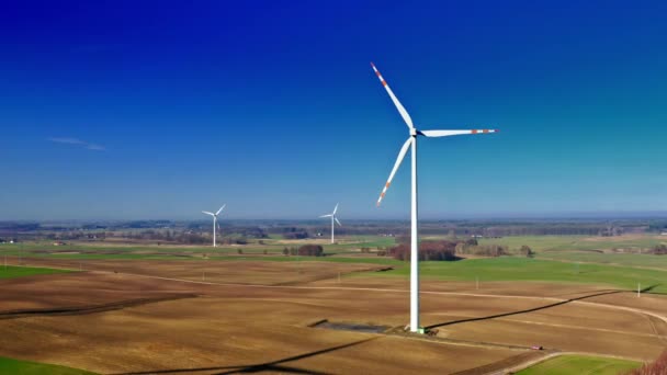Белая ветряная турбина на коричневом поле с голубым небом, вид с воздуха — стоковое видео