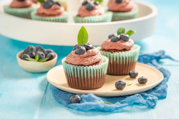 Babeczki z kremem czekoladowym i jagodami na niebieskim stole — Zdjęcie stockowe