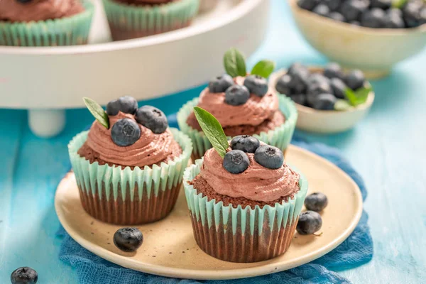 Babeczki z kremem czekoladowym i jagód na niebieskim stole — Zdjęcie stockowe