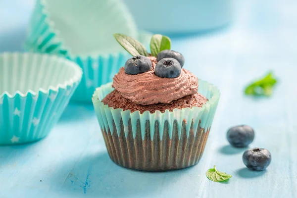 Cupcake z kremu czekoladowego i jagód na niebieskim stole — Zdjęcie stockowe
