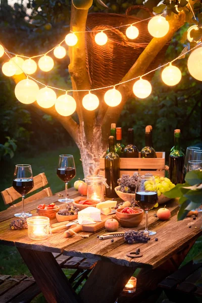 Closeup of table with appetizers and wine in illuminated garden — Stock Photo, Image